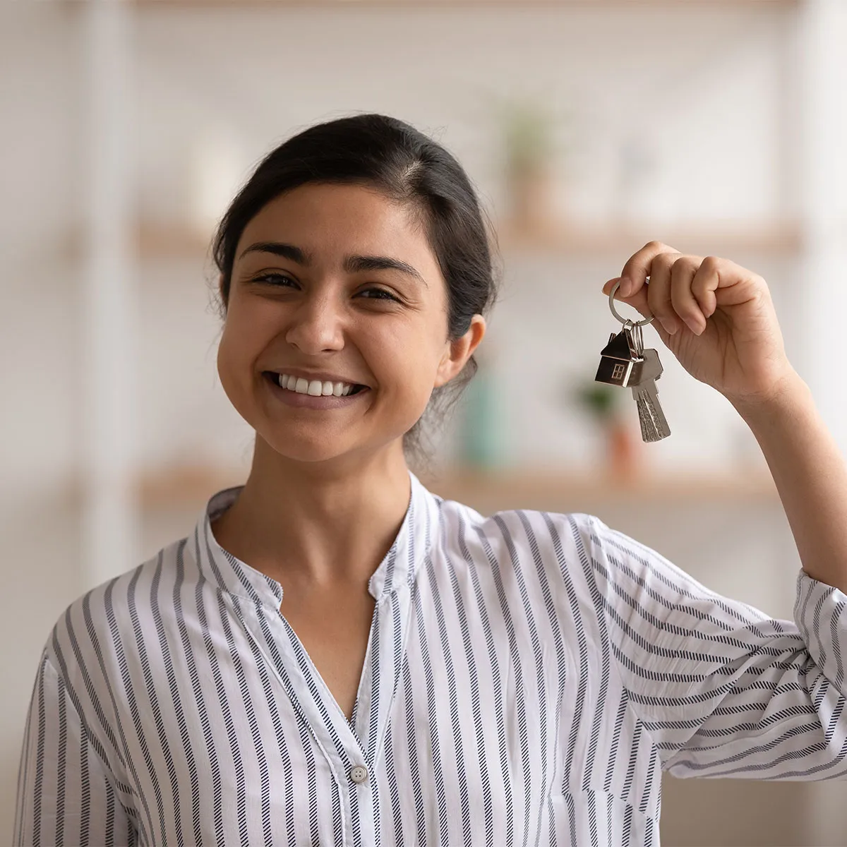 A person smiling holding up keys to their new home after getting a new home loan with the help of a financial advisor.