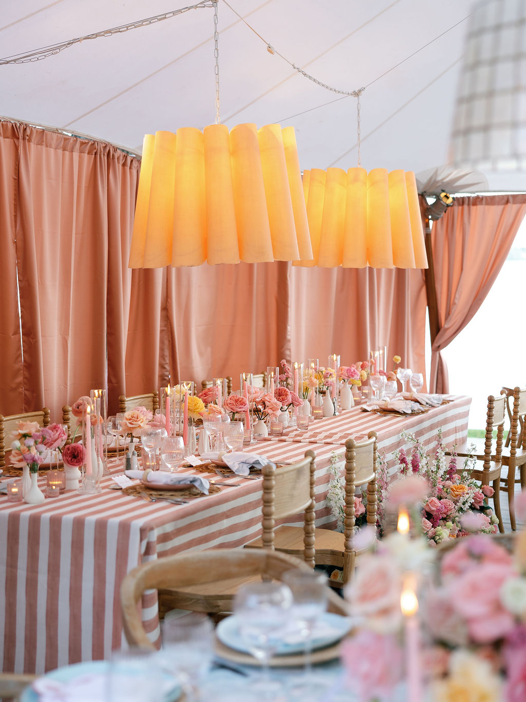 Candlelit reception tablescape with pink-and-white striped linens, garden roses, and warm pendant lighting under the tent at a Lorton, Virginia wedding.