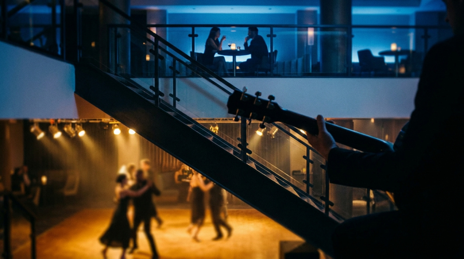 A guitarist's hand rests on his instrument where a staircase divides a lit dance floor from a hushed lounge.