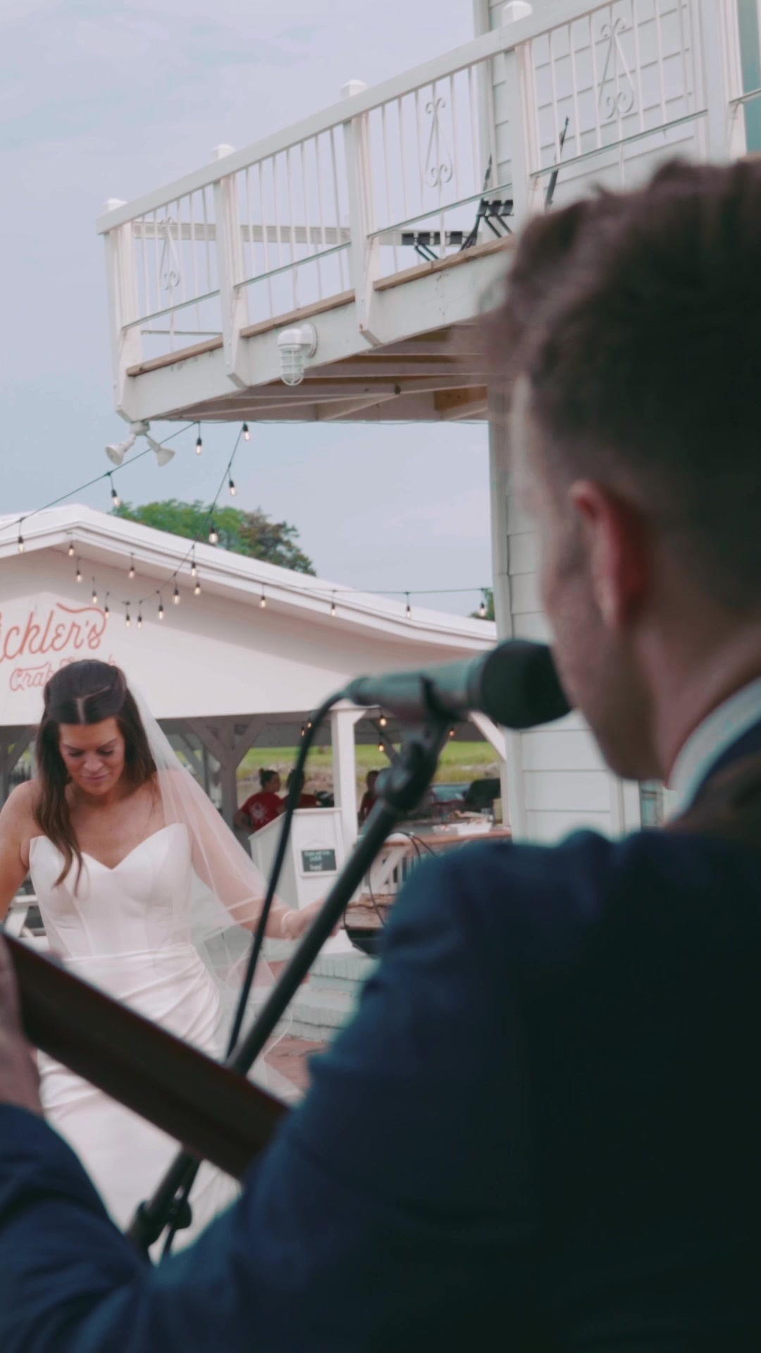 A wedding guitarist performing as the bride stands on the waterfront deck at Wylder Hotel, Tilghman Island, Maryland.