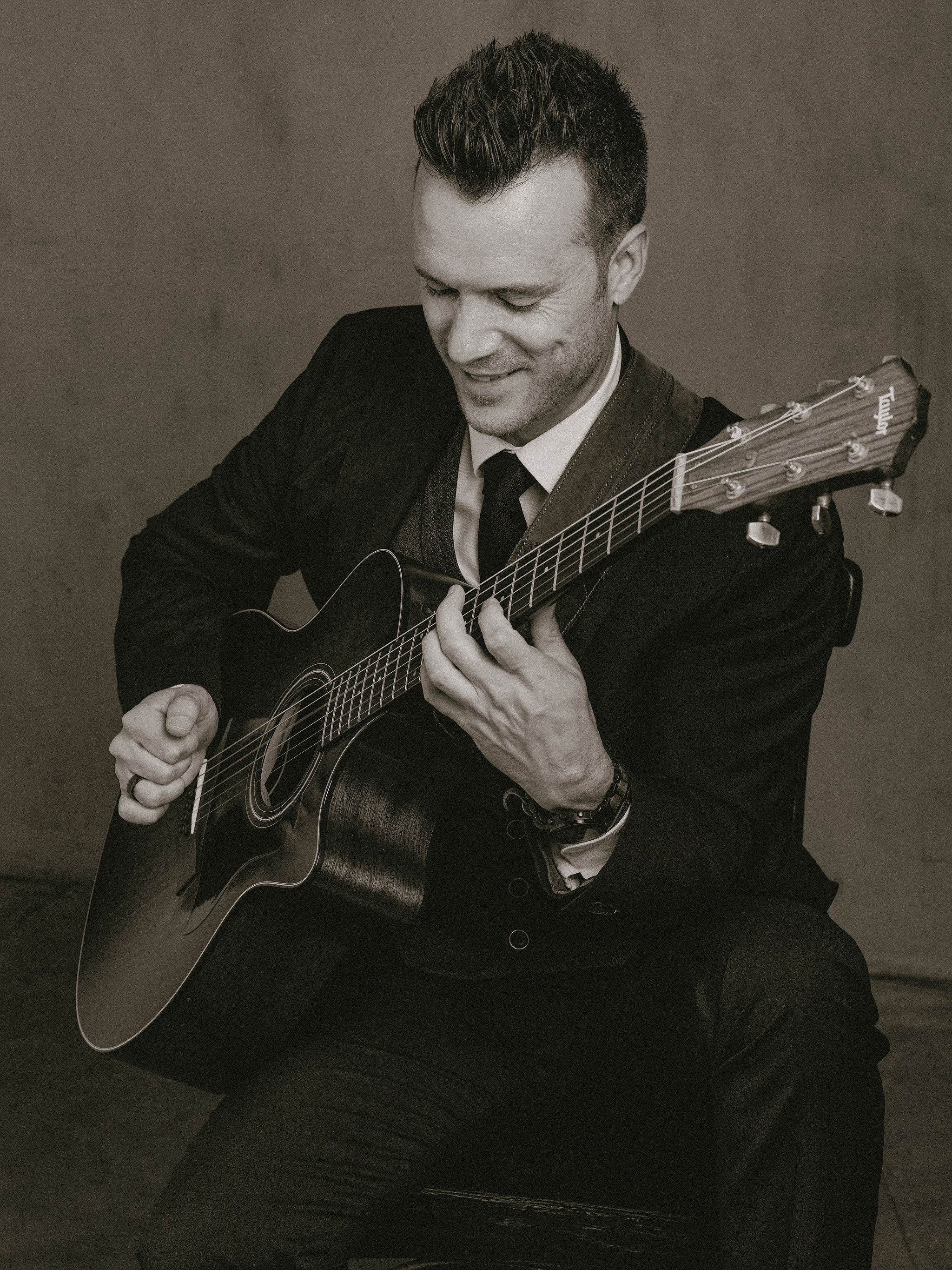 A wedding singer and acoustic guitarist smiling mid-performance in a black-and-white studio portrait.