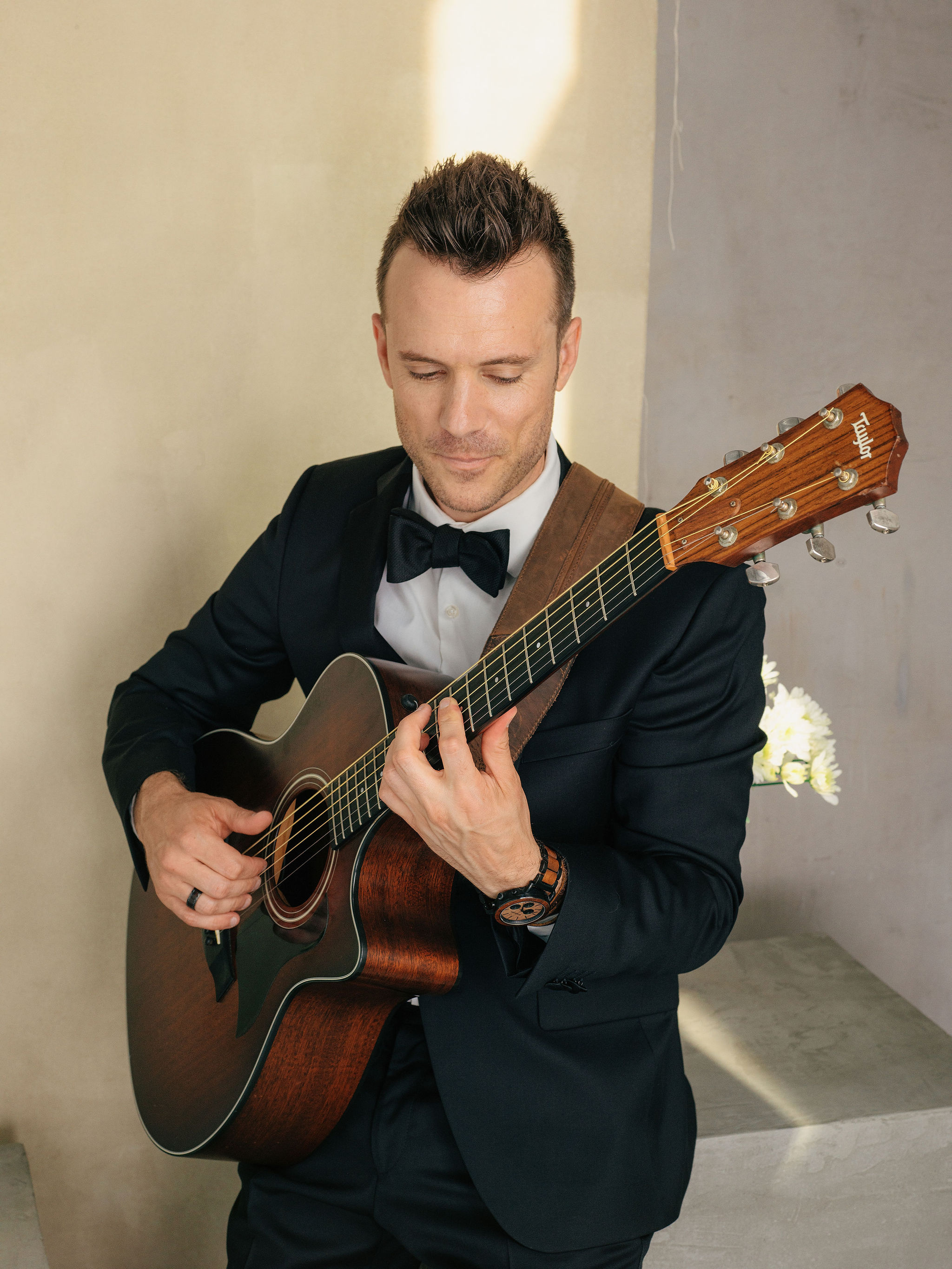 A solo wedding musician in a tuxedo playing an acoustic guitar in a formal portrait setting