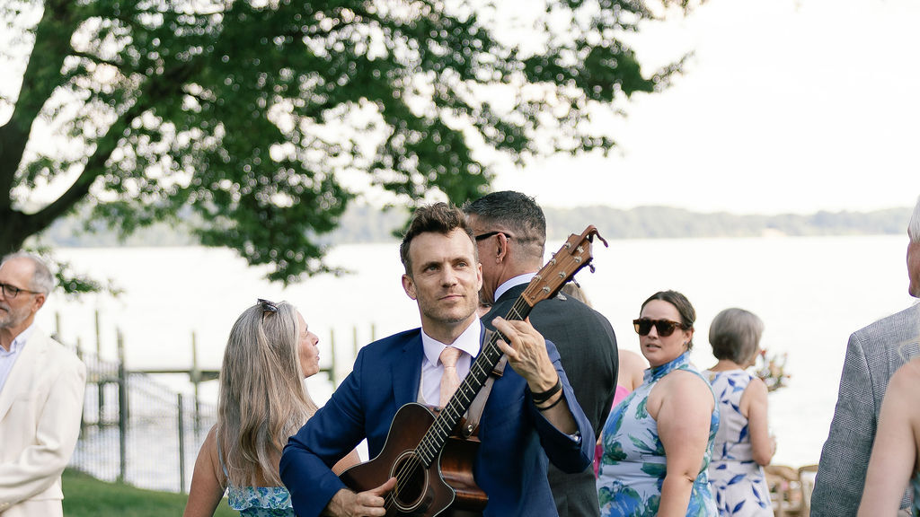 A guitarist performs live for guests gathered outdoors during an evening cocktail hour