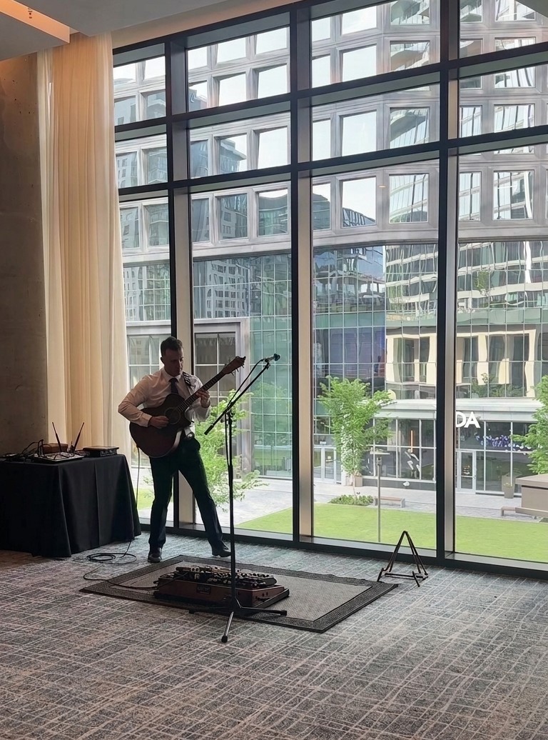 A solo guitarist plays at a JW Marriott Reston corporate event, pedal board at his feet, mixer on a side table.