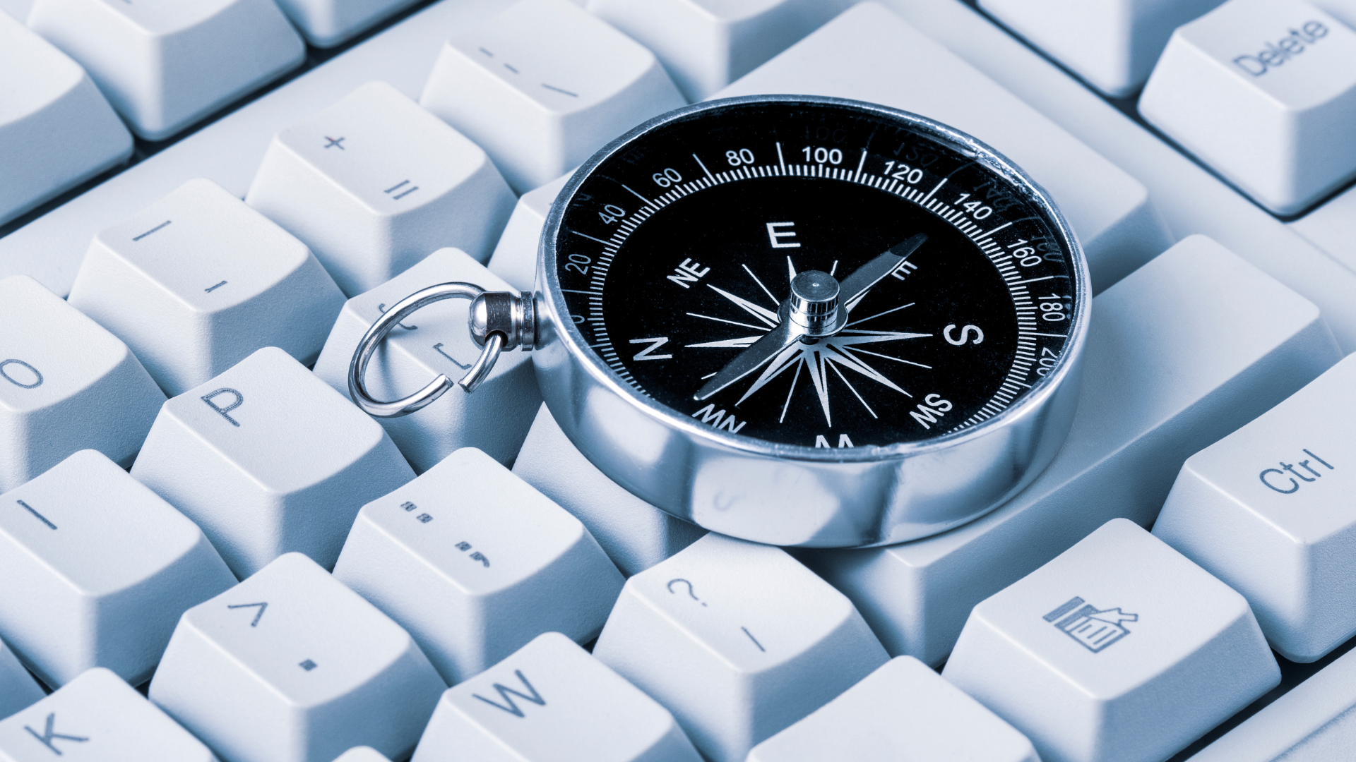A compass pointing east sitting atop a white computer keyboard