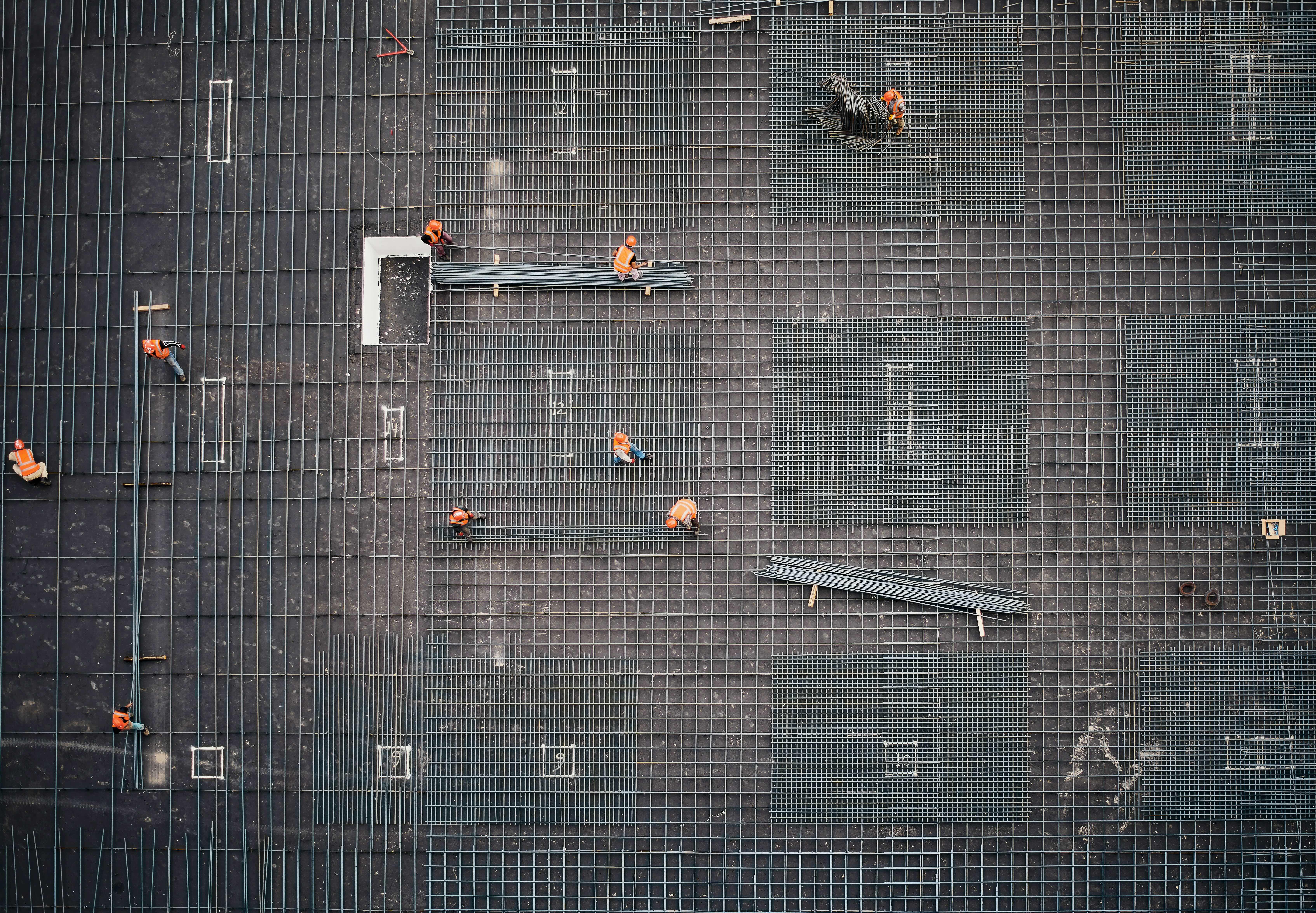 Aerial view of construction workers in orange vests working on steel rebar grid at a building site.