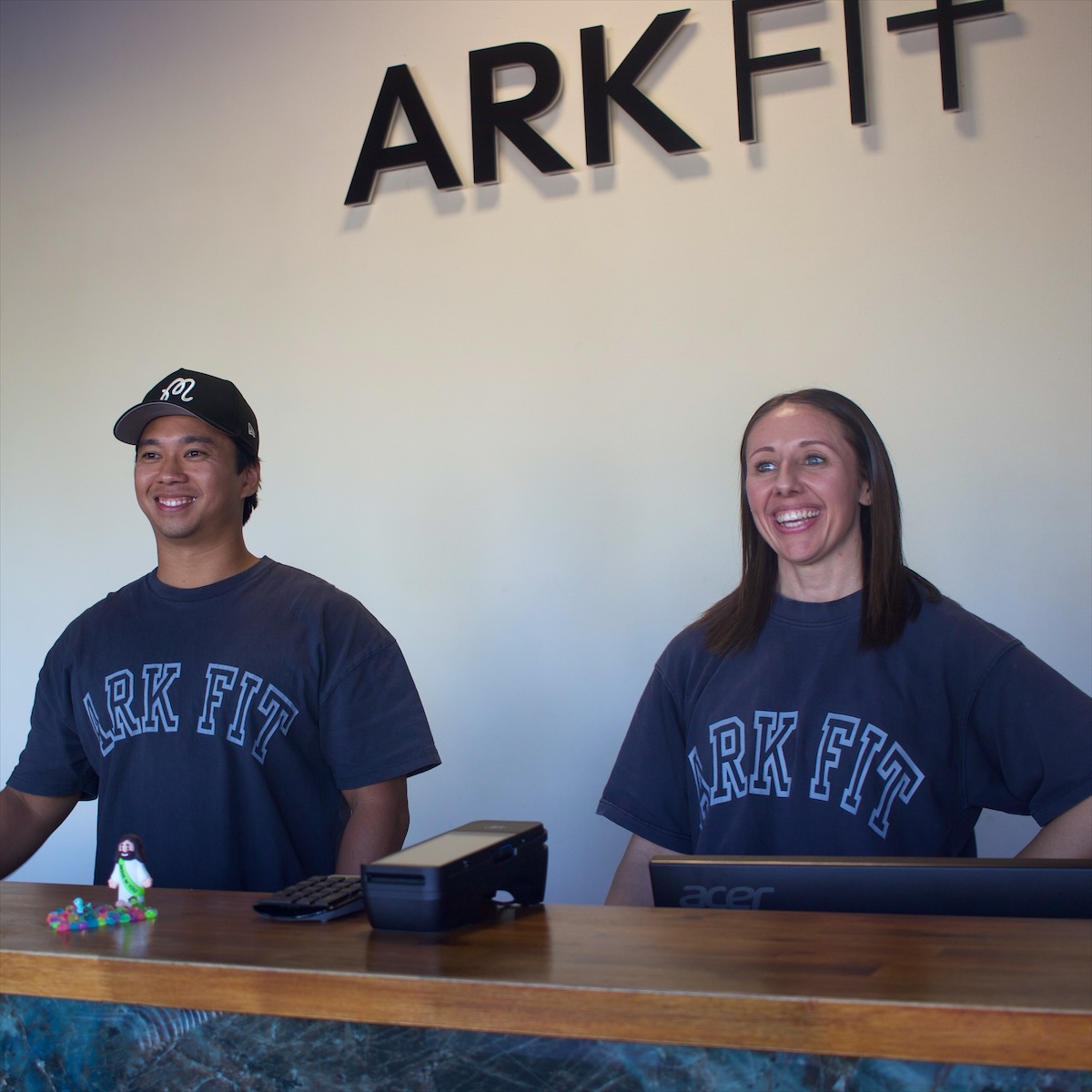 Smiling Ark Fit staff at the front desk under the Ark Fit sign