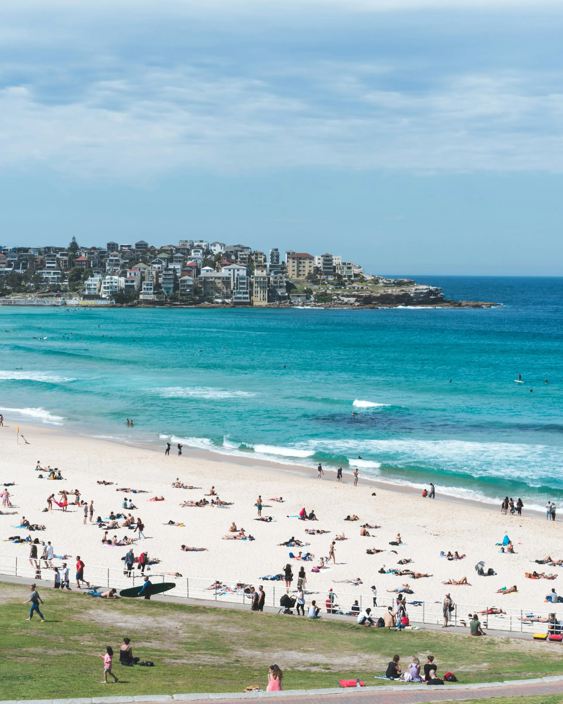 Bondi Beach on a sunny day, with people relaxing on the sand and swimmers in the turquoise waves.