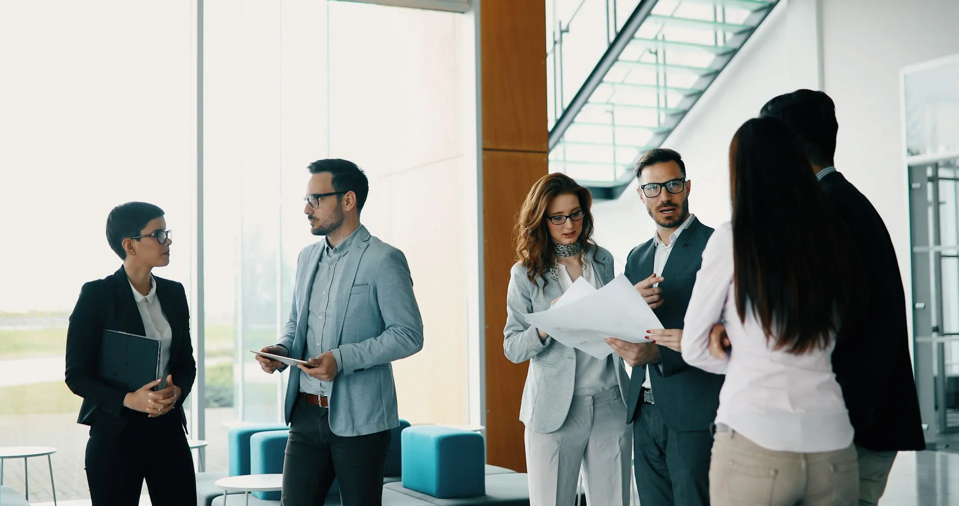 Group of professionals standing in a bright, modern office lobby discussing documents and schedules, representing seamless coordination and planning for group transport needs.