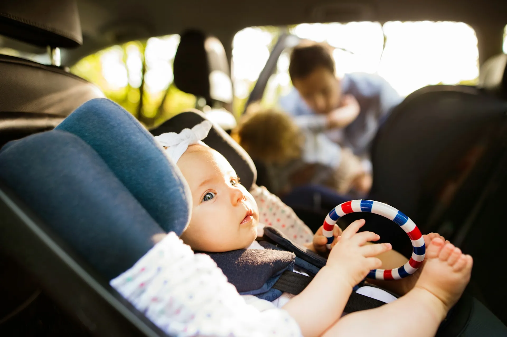 A baby securely fastened in a rear-facing car seat, playing with a toy while a parent tends to another child in the background, highlighting Evoke’s focus on safe, family-friendly transfers across Australia.