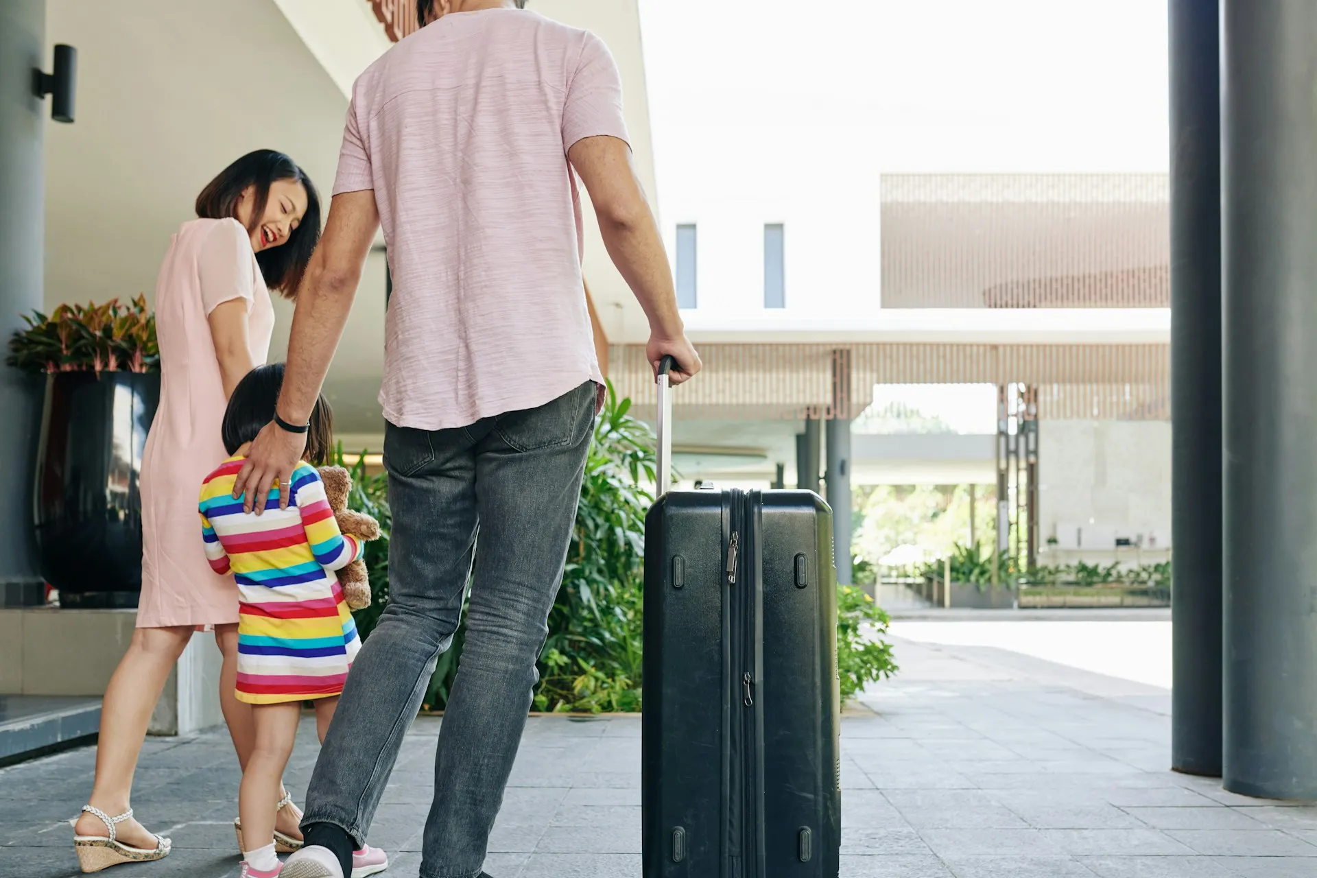 A young family arriving at a modern building with a suitcase and a teddy bear in hand, illustrating Evoke’s flexible, family-focused service that adapts to your travel needs and schedule.