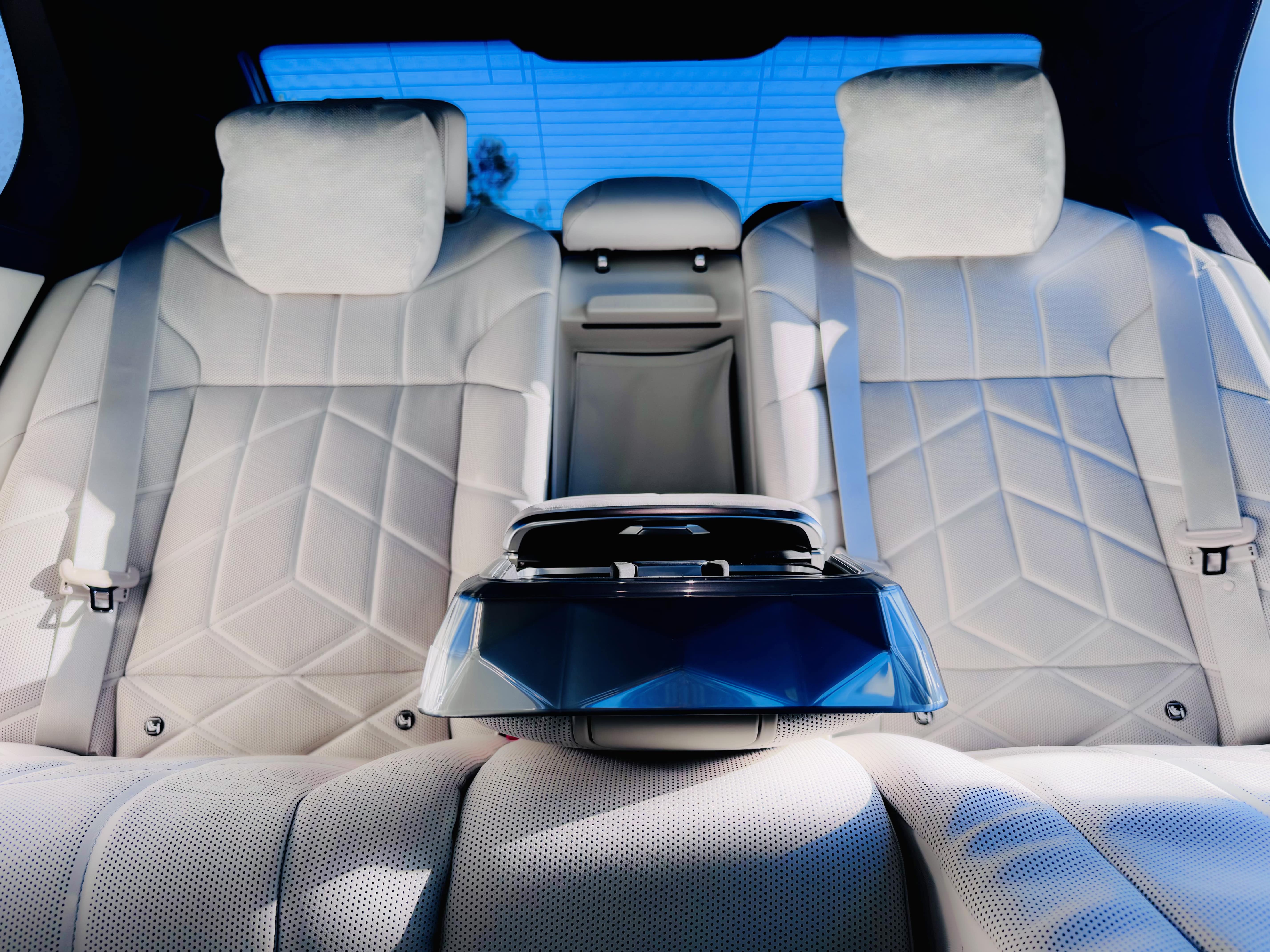 Rear seats of the BMW i7 with light leather upholstery, geometric stitching, plush headrests, and a closed centre armrest with a glossy finish.