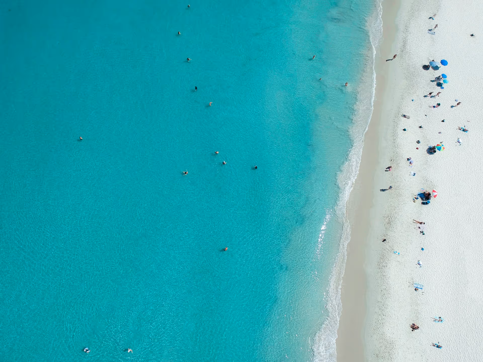 Aerial view of Port Beach in North Fremantle, Perth, Western Australia, showing turquoise water, white sand, and beachgoers under umbrellas.