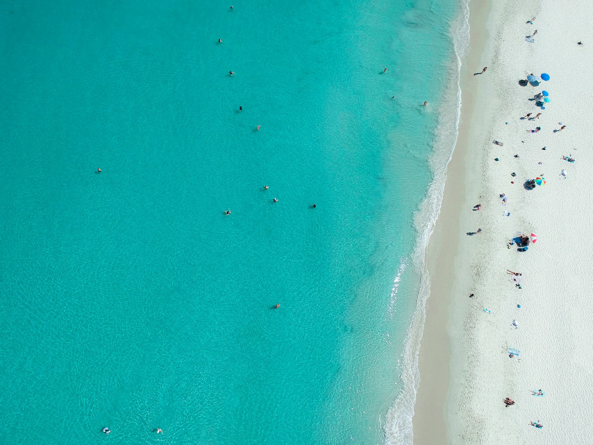 Aerial view of Port Beach in North Fremantle, Perth, Western Australia, showing turquoise water, white sand, and beachgoers under umbrellas.