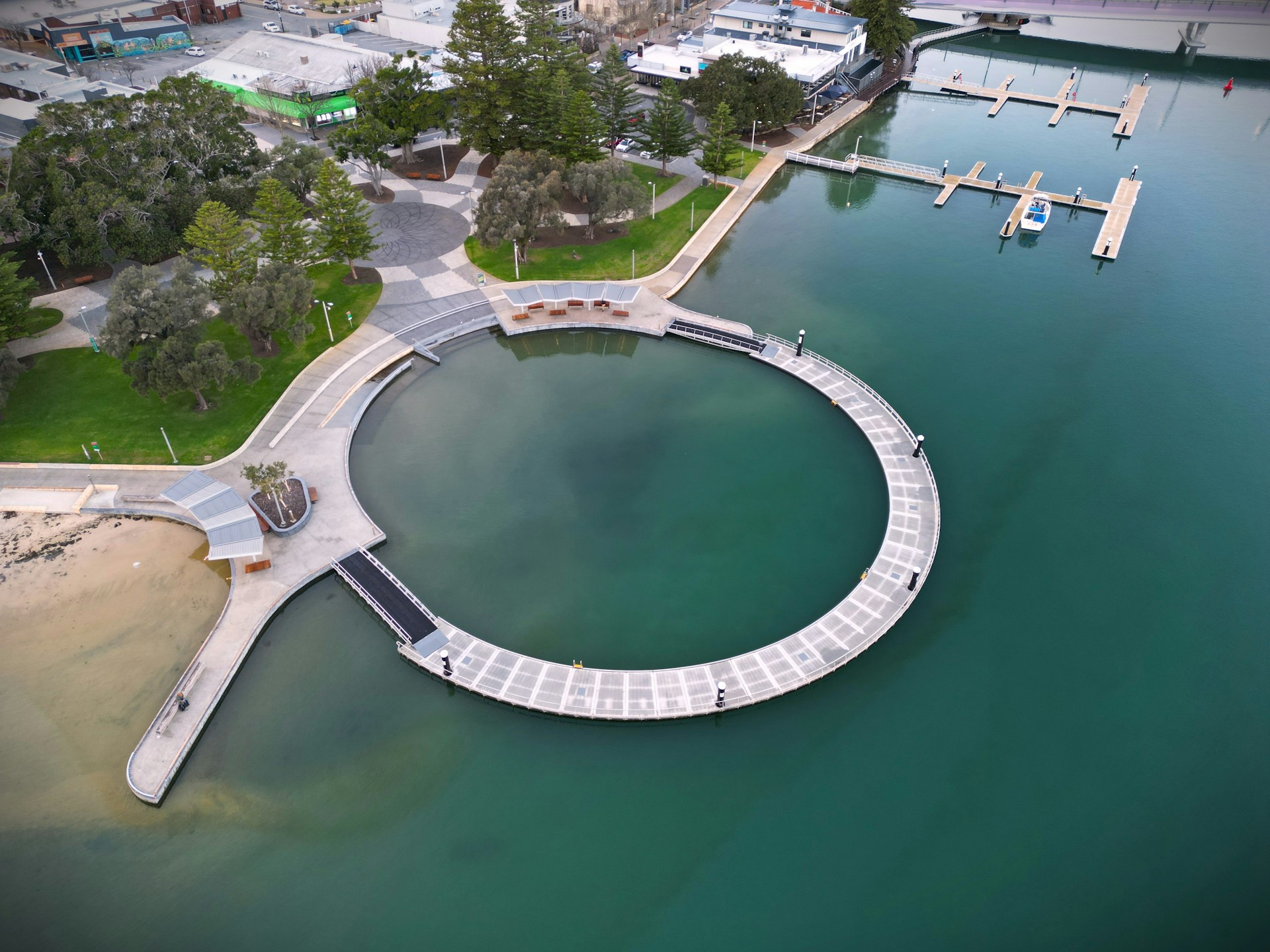 Aerial view of the circular boardwalk and marina in Mandurah, Western Australia, with surrounding parkland and waterfront buildings.
