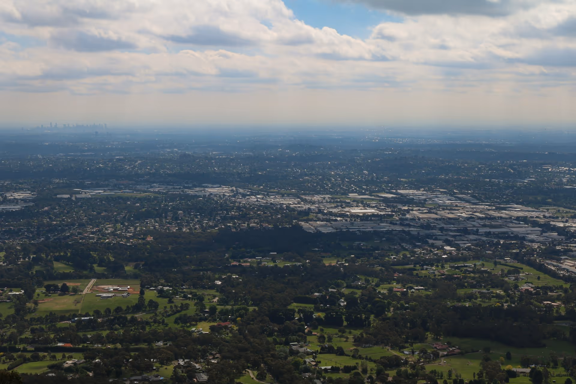 View of Melbourne’s skyline in the distance with the Eastern Suburbs and green landscapes seen from Burkes Lookout in the Dandenong Ranges.