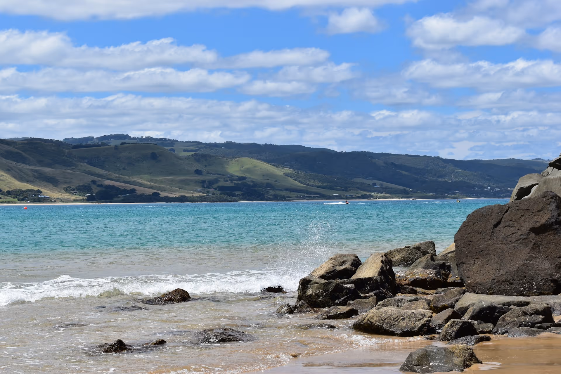 Rocky shoreline at Apollo Bay with turquoise waters and rolling green hills in the background.