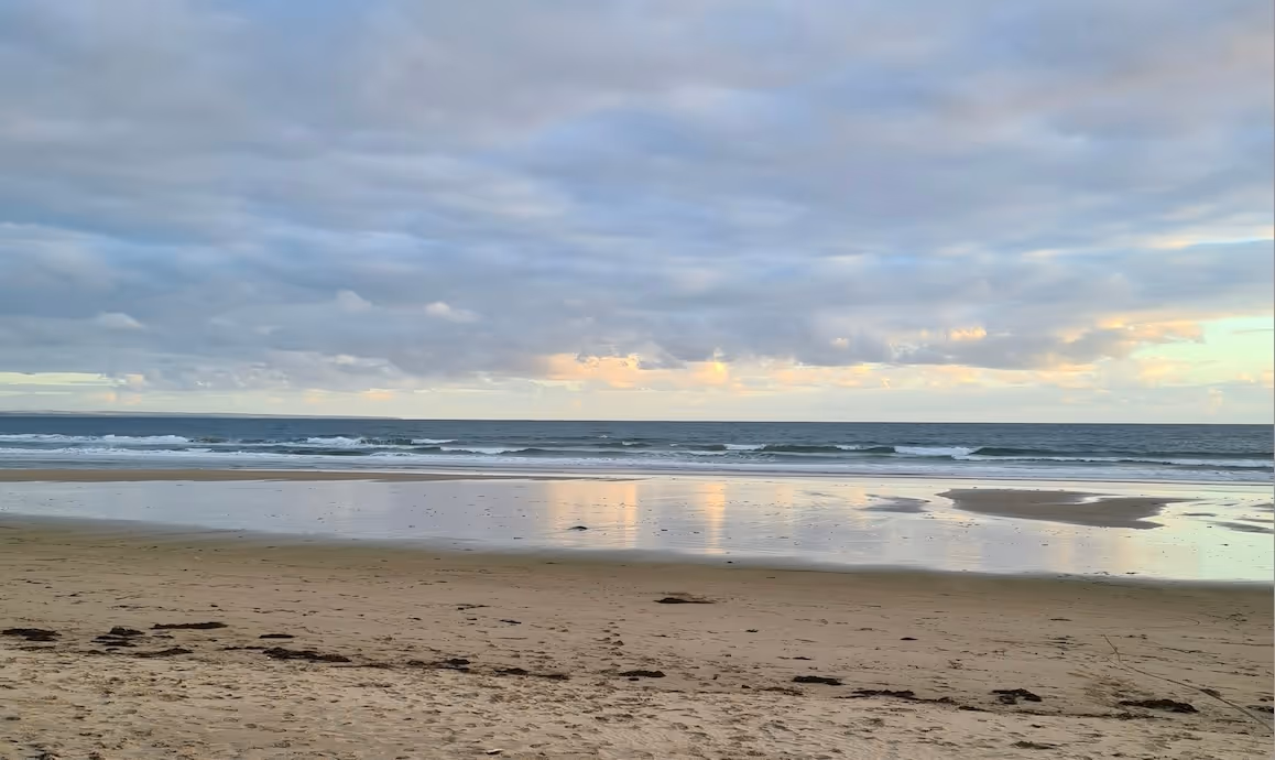 Calm waves rolling onto the sandy shore at Inverloch Beach, Victoria, under a cloudy sky.