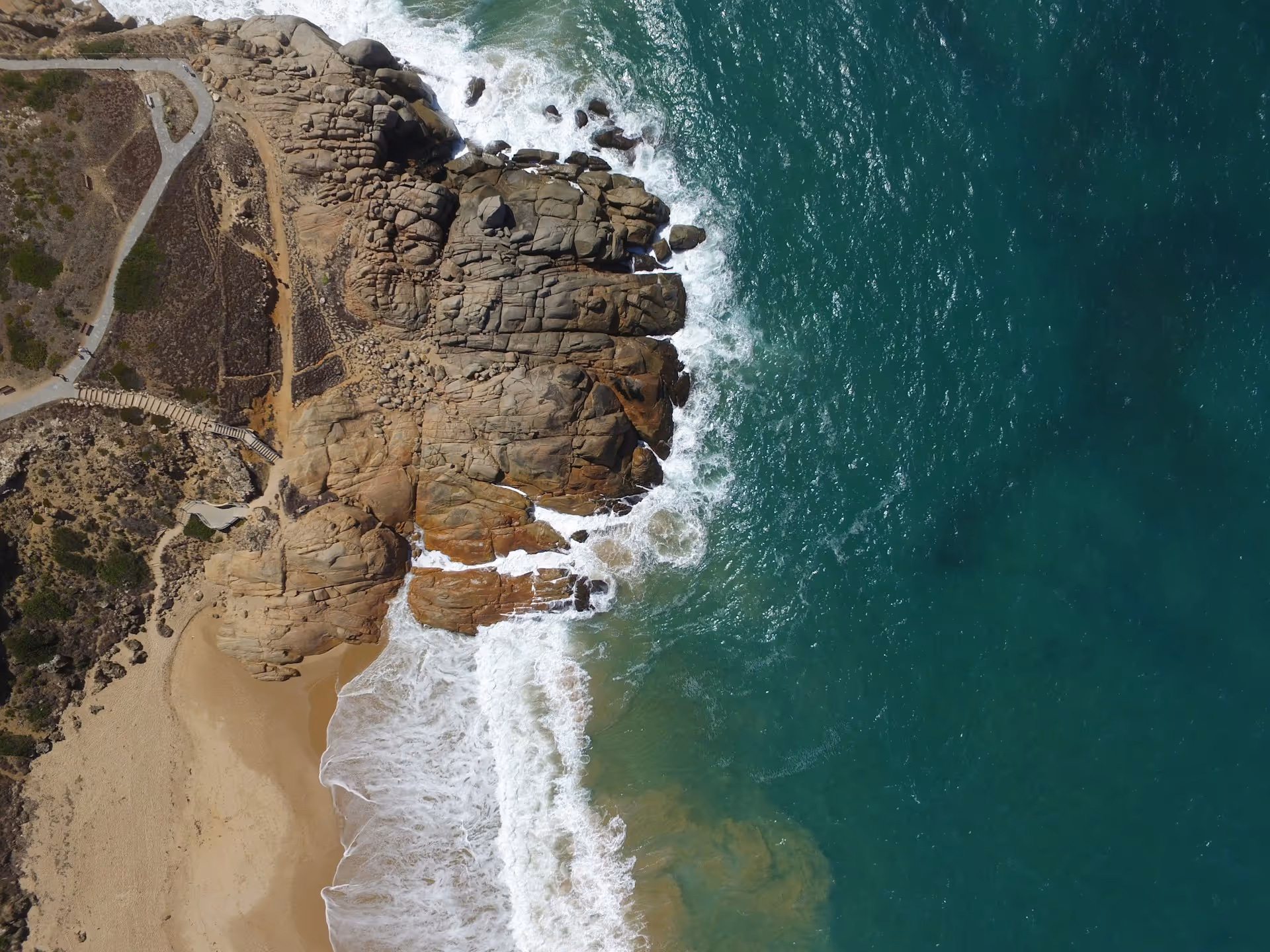 Aerial view of Port Elliot’s rocky coastline with waves crashing against the cliffs, sandy beach below, and turquoise waters stretching out to sea.