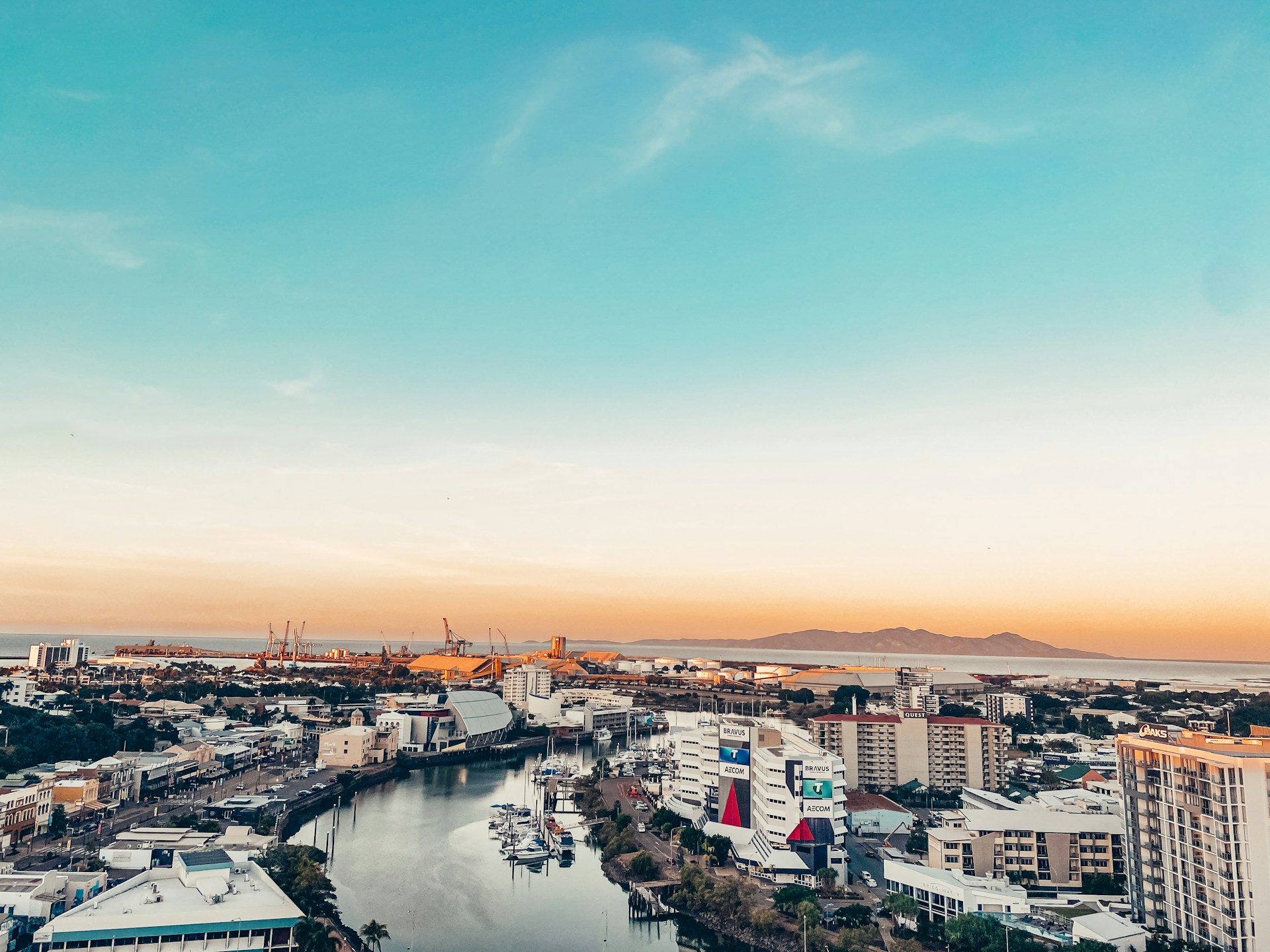 Aerial view of Townsville at sunset, showing the marina, city buildings, and Magnetic Island in the distance.
