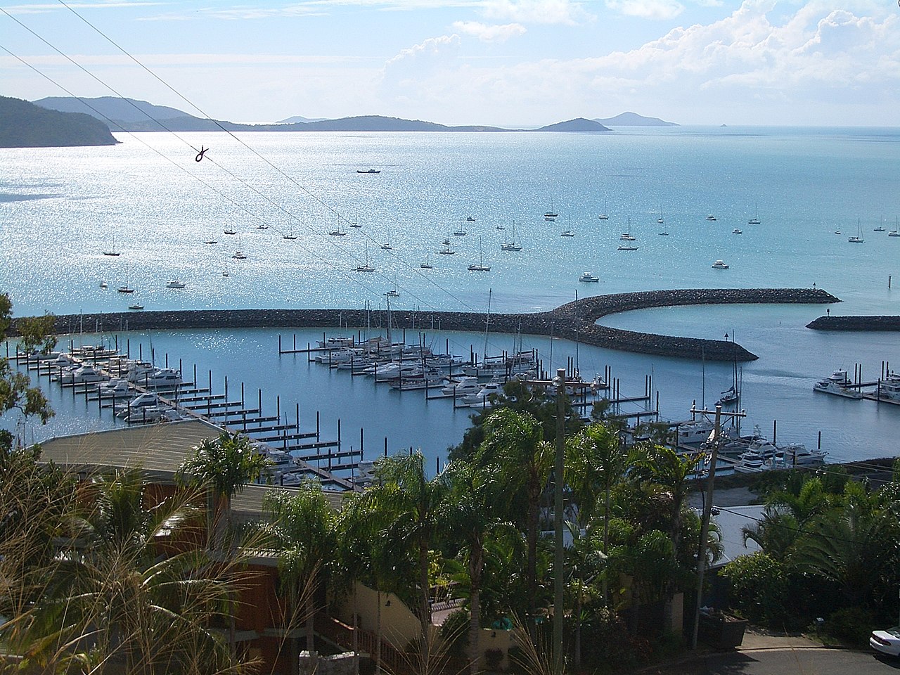 Harbour at Airlie Beach with boats anchored in turquoise water under a blue sky. Credit: Vmenkov, Wikimedia Commons: https://commons.wikimedia.org/wiki/File:Airlie-Beach-harbor-1286.jpg
