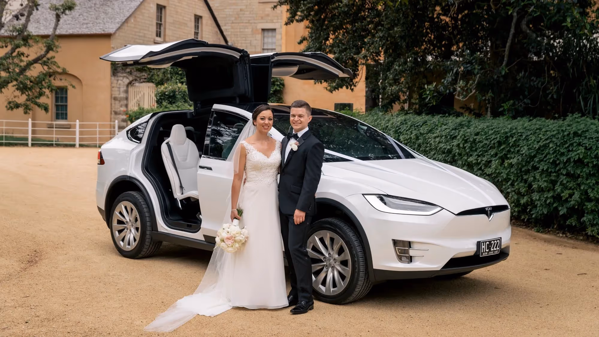 Bride and groom standing in front of Tesla Model X with falcon wing doors open.
