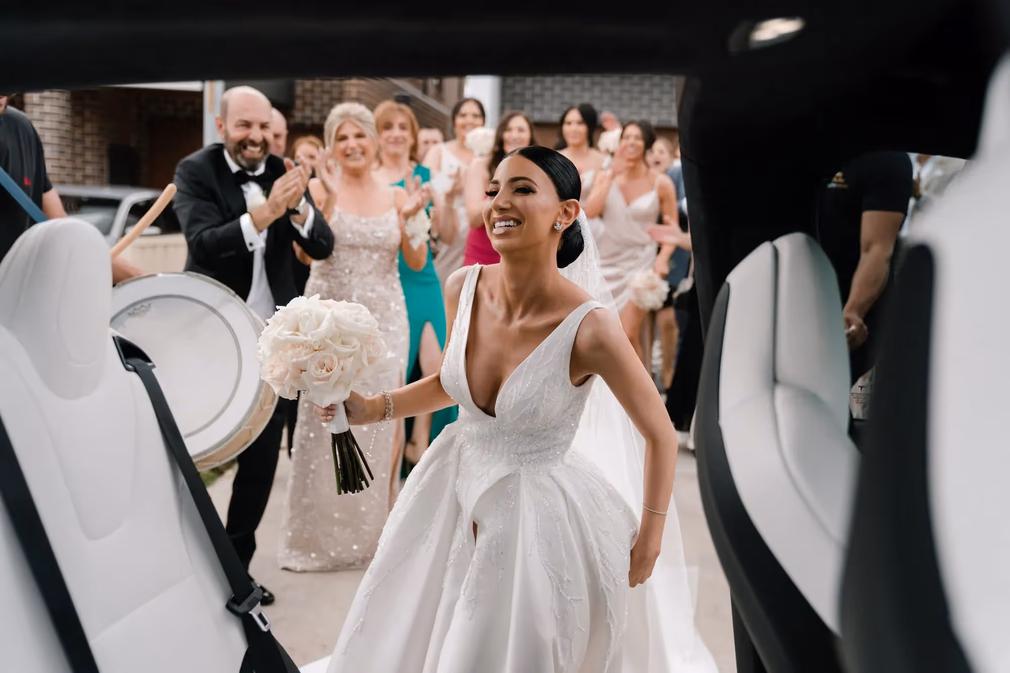 Bride entering Tesla Model X with falcon wing door open and guests clapping in the background.