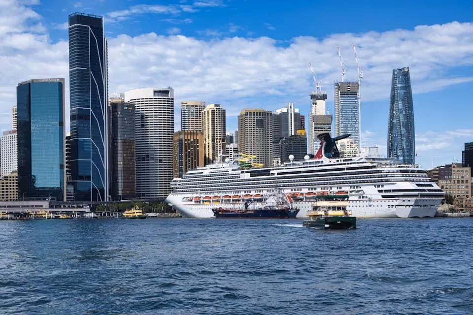 Sydney Harbour with a view of a cruise ship docked, surrounded by modern skyscrapers and the city skyline.