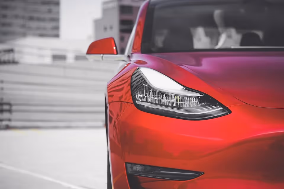 Close-up of the front headlight and sleek design of a red Tesla Model 3, showcasing its modern and aerodynamic features.