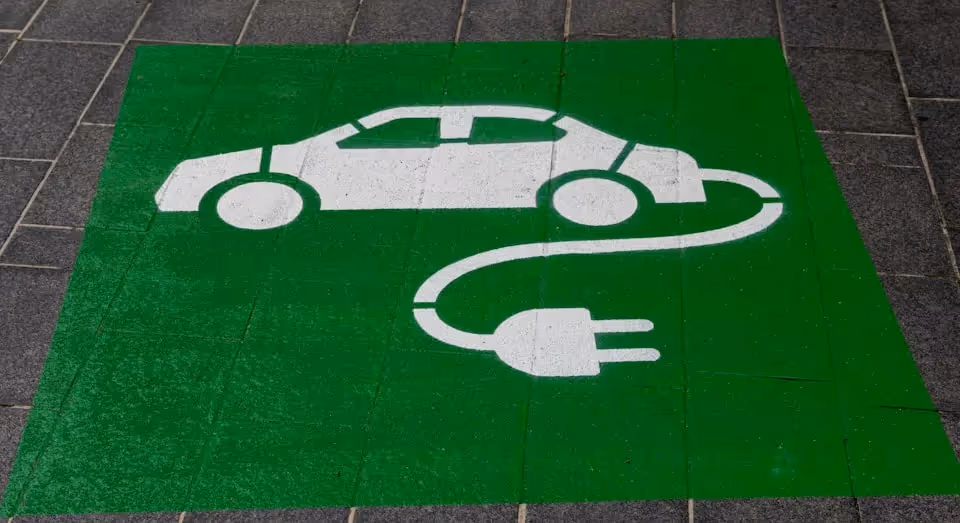 Green painted parking space with a white symbol of an electric car connected to a charging plug, indicating a designated area for electric vehicle charging.