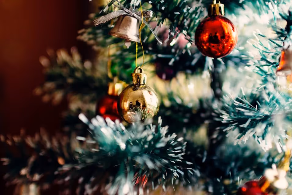 Close-up of a Christmas tree adorned with red and gold baubles, silver bells, and green tinsel, capturing the festive holiday spirit.