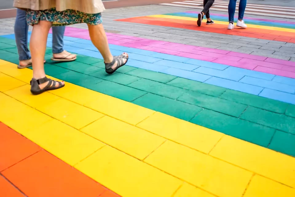 People walking across a colourful rainbow-painted crosswalk, representing LGBTQIA+ pride.