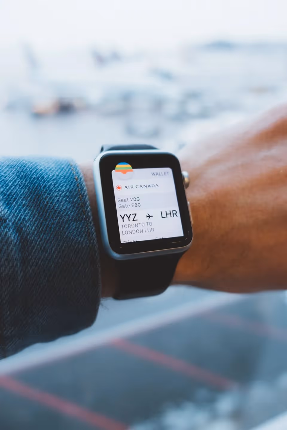 A person wearing a smartwatch displaying an Air Canada boarding pass for a flight from Toronto (YYZ) to London (LHR), with an airport runway visible in the blurred background.