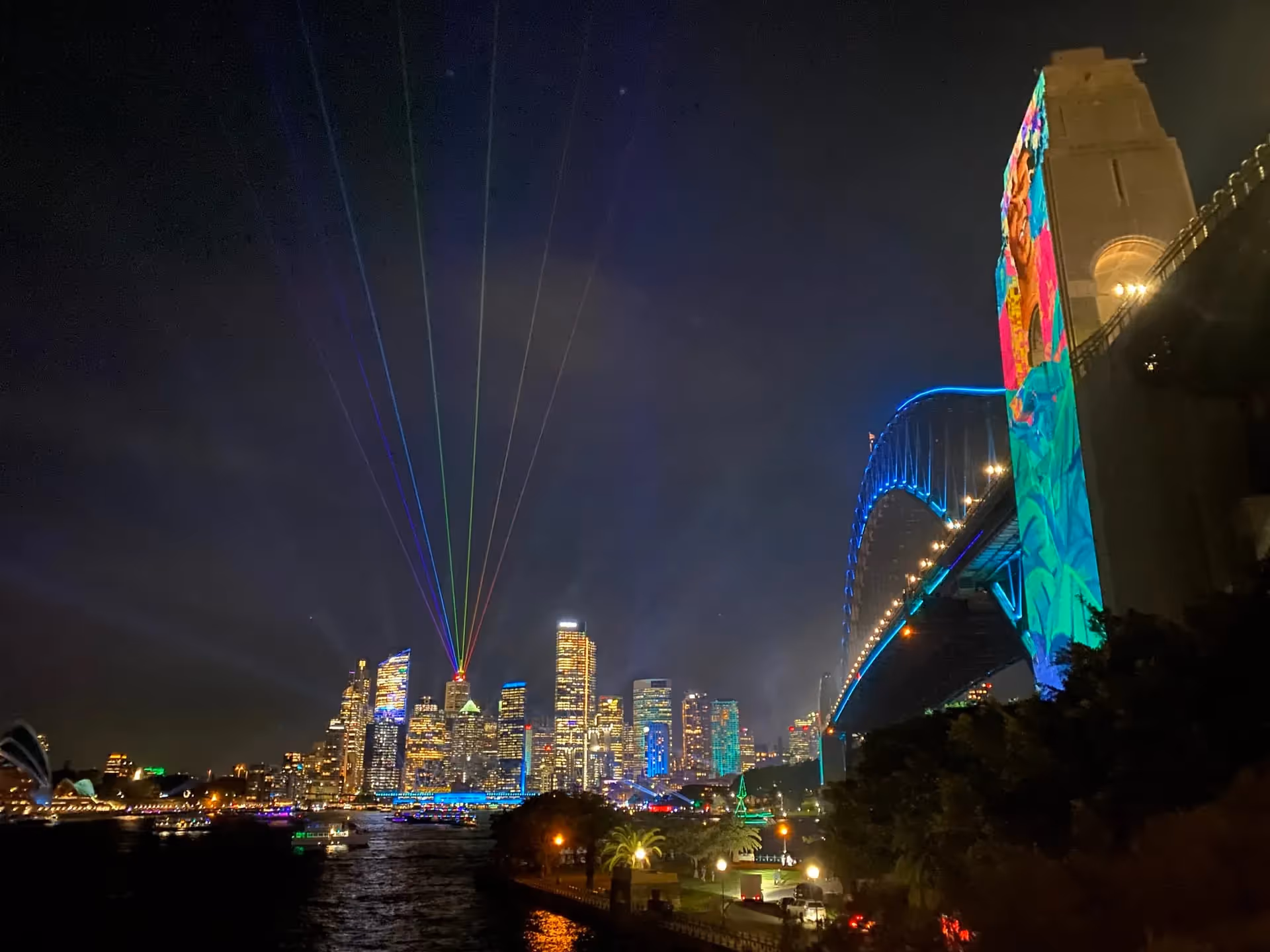 Sydney's Vivid 2024 festival at night with the Harbour Bridge illuminated by light projections and laser beams.