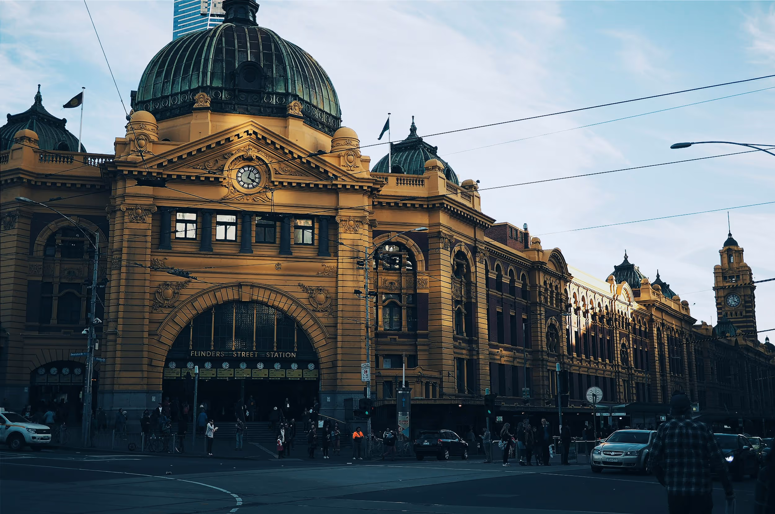 Flinders Street Station in Melbourne with its iconic yellow facade, central dome, clock, and bustling entrance, surrounded by trams and cars.