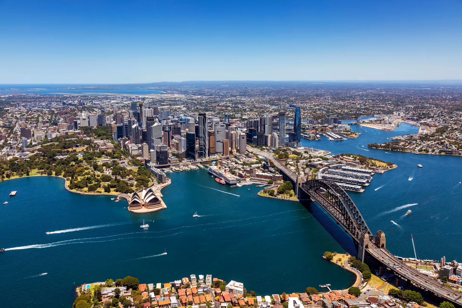 Aerial view of Sydney, showcasing the Sydney Opera House, Sydney Harbour Bridge, and the city's central business district.