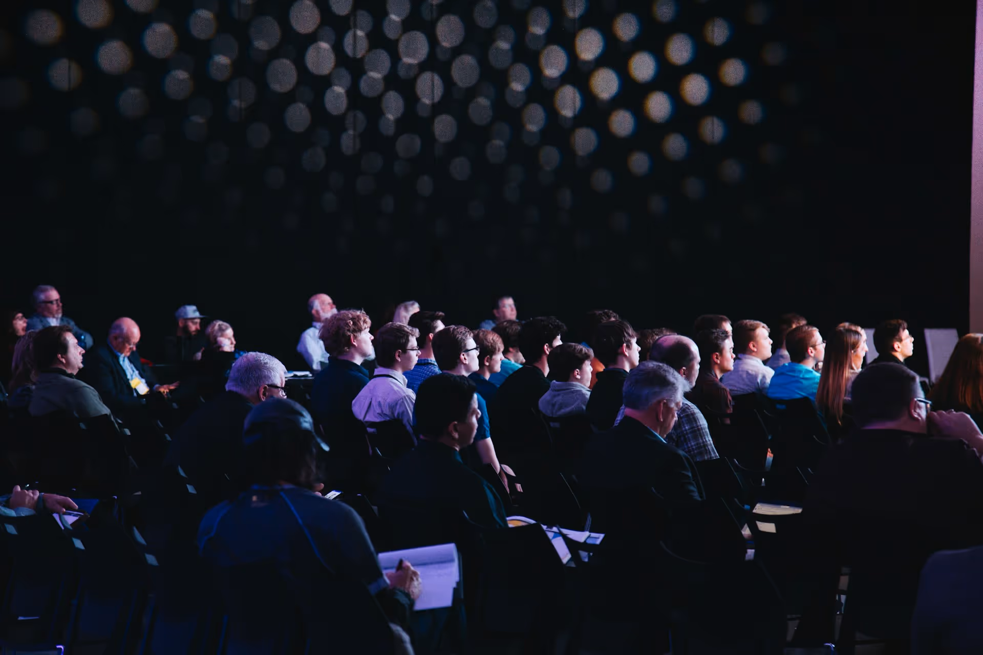 A large group of people seated in a conference room, watching a presentation.