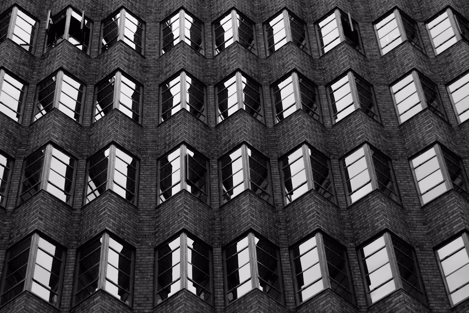 A black and white image of a building facade featuring repeating patterns of angled windows
