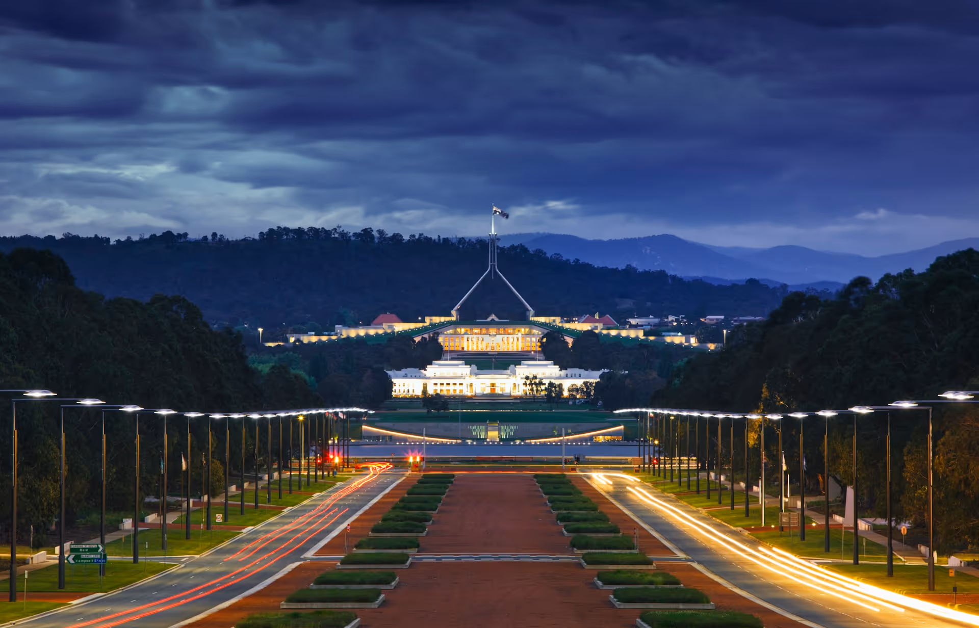 Evening view of Canberra’s Parliament House with illuminated roadways leading into the city, highlighting a key intercity chauffeur route between Sydney and the Australian Capital Territory.
