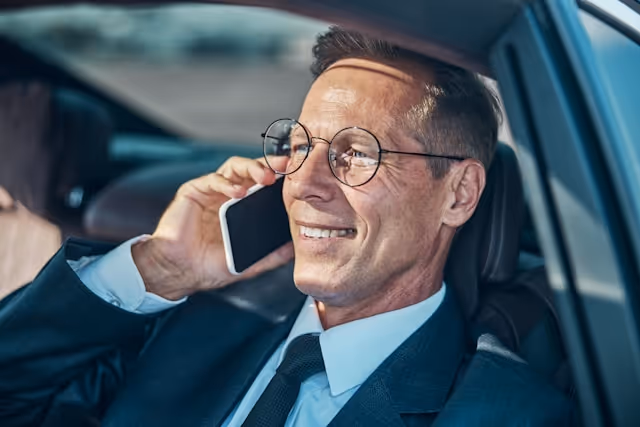 A businessman sits in the back of a car, talking on his mobile phone during a private chauffeur-driven ride.
