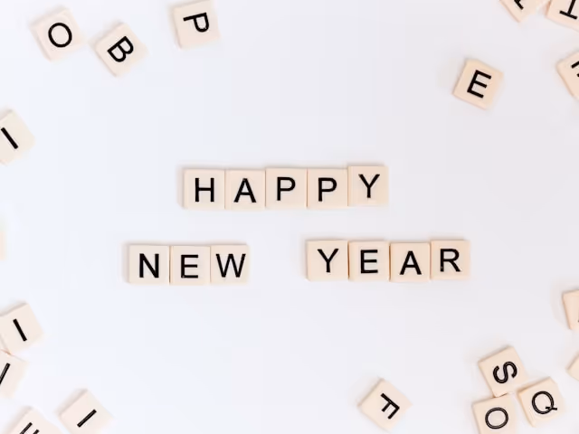 Scrabble tiles arranged to spell 'Happy New Year' on a white background, with scattered letters around.
