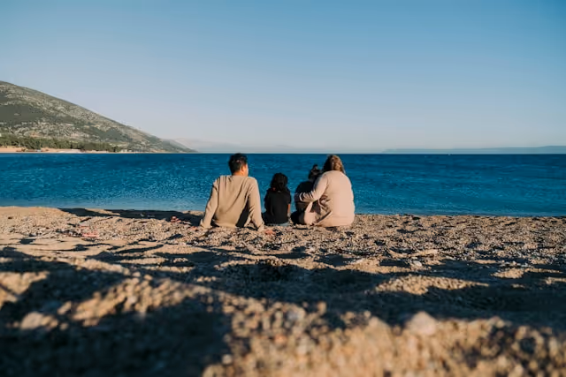 A family sits together on a quiet beach, enjoying a relaxed and peaceful moment by the water.