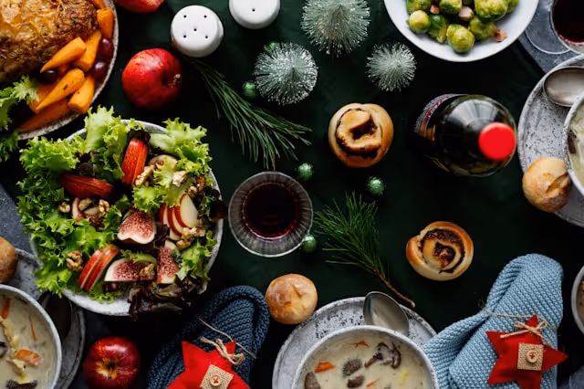 A festive dining table with a variety of dishes, including a fresh salad, roasted vegetables, bread rolls, and holiday decorations.