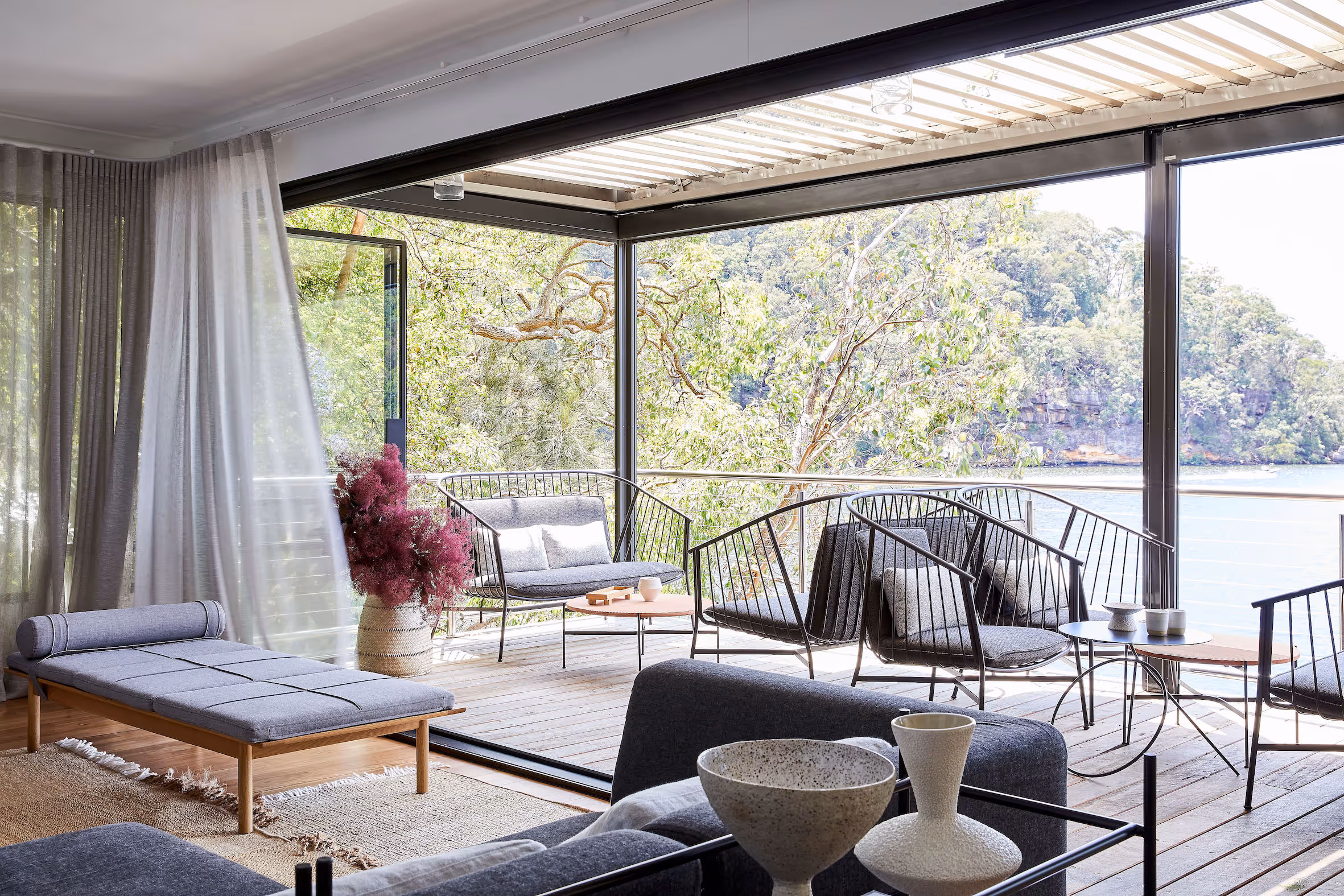 Modern and stylish open-plan living space at Calabash Bay Lodge, featuring floor-to-ceiling windows, contemporary furnishings, and a scenic waterfront view surrounded by lush greenery.