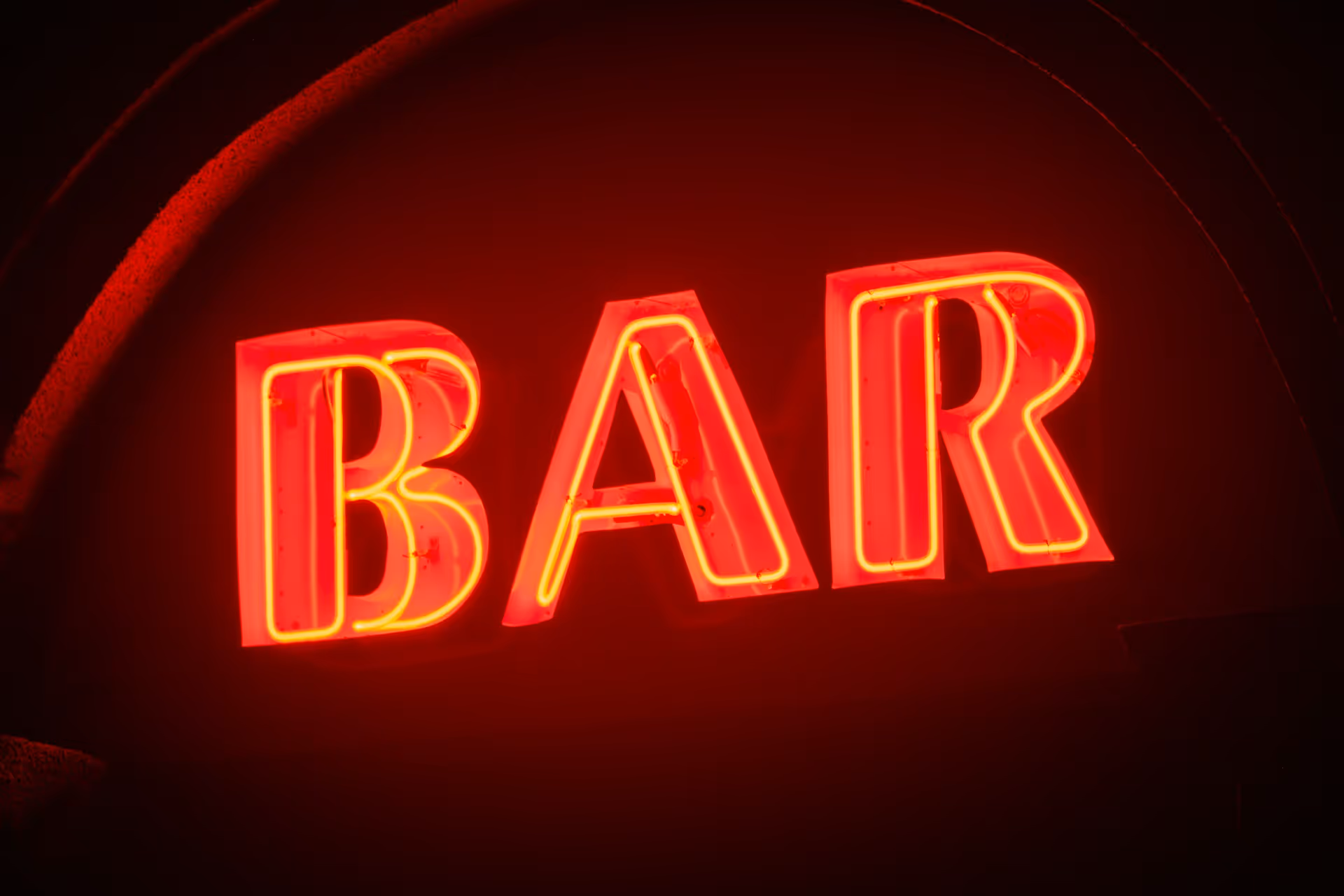 A glowing red neon sign displaying the word "BAR" against a dark background.