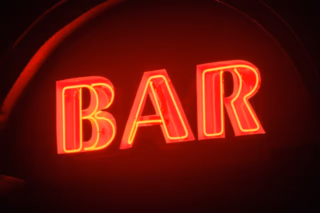 A glowing red neon sign displaying the word "BAR" against a dark background.