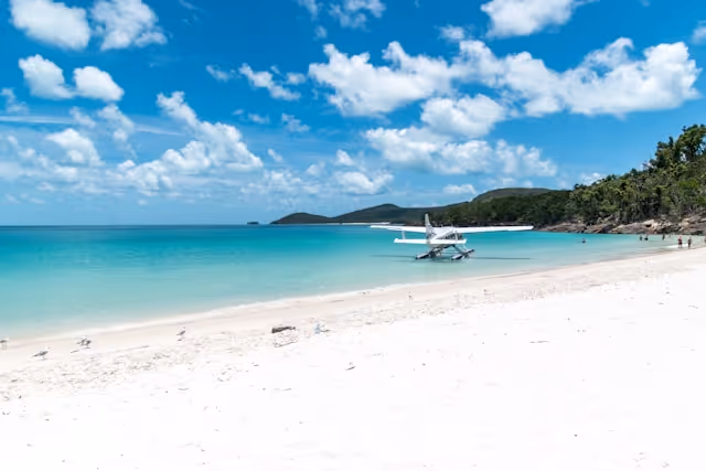 Hamilton Island beach with its pristine white sand and turquoise waters, featuring a seaplane docked at the shore.