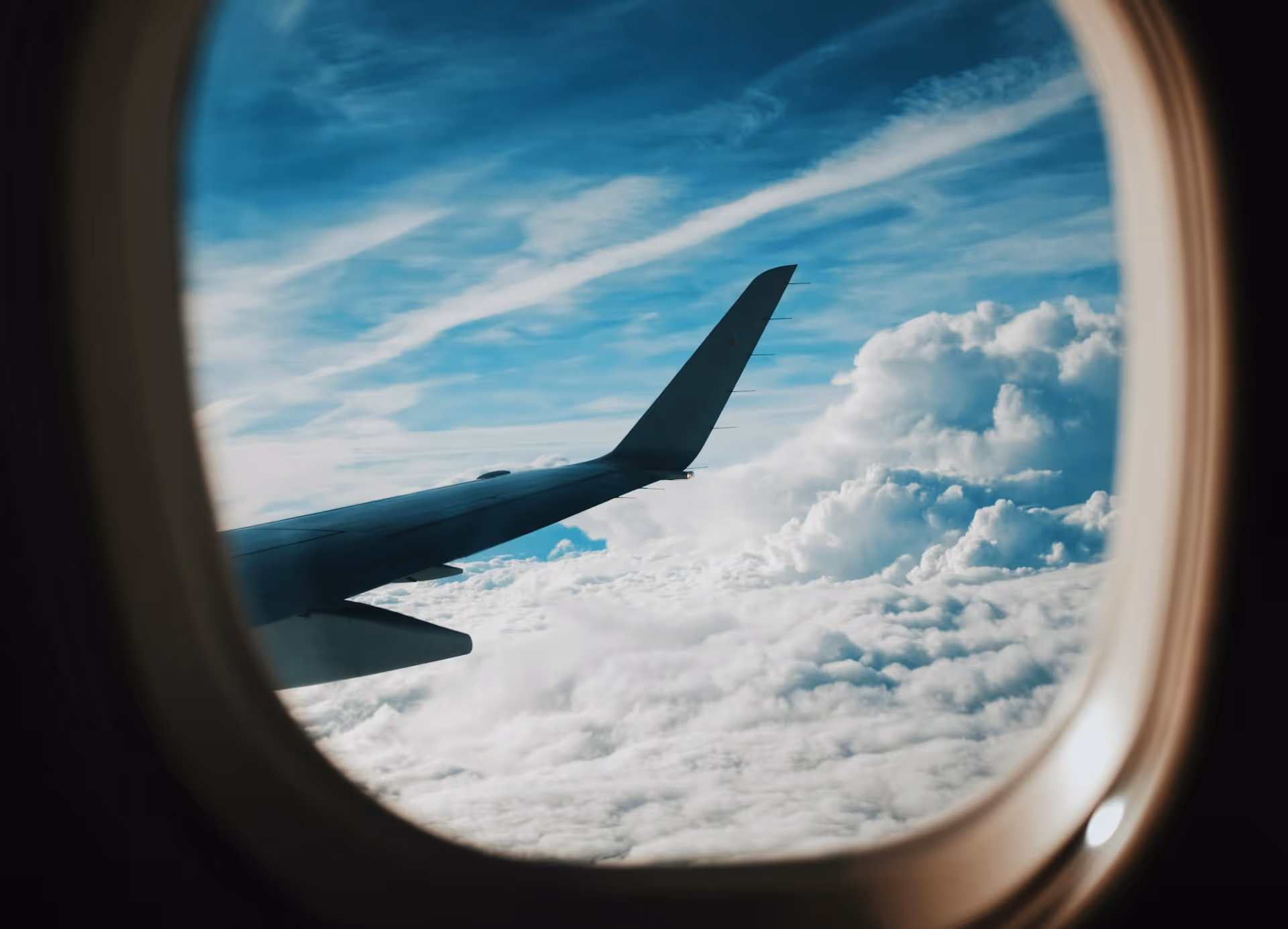 A view from an airplane window showing the aircraft wing soaring above the clouds against a blue sky