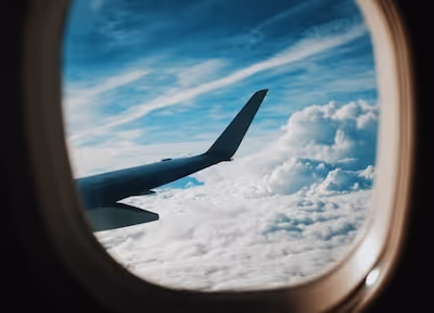 A view from an airplane window showing the aircraft wing soaring above the clouds against a blue sky