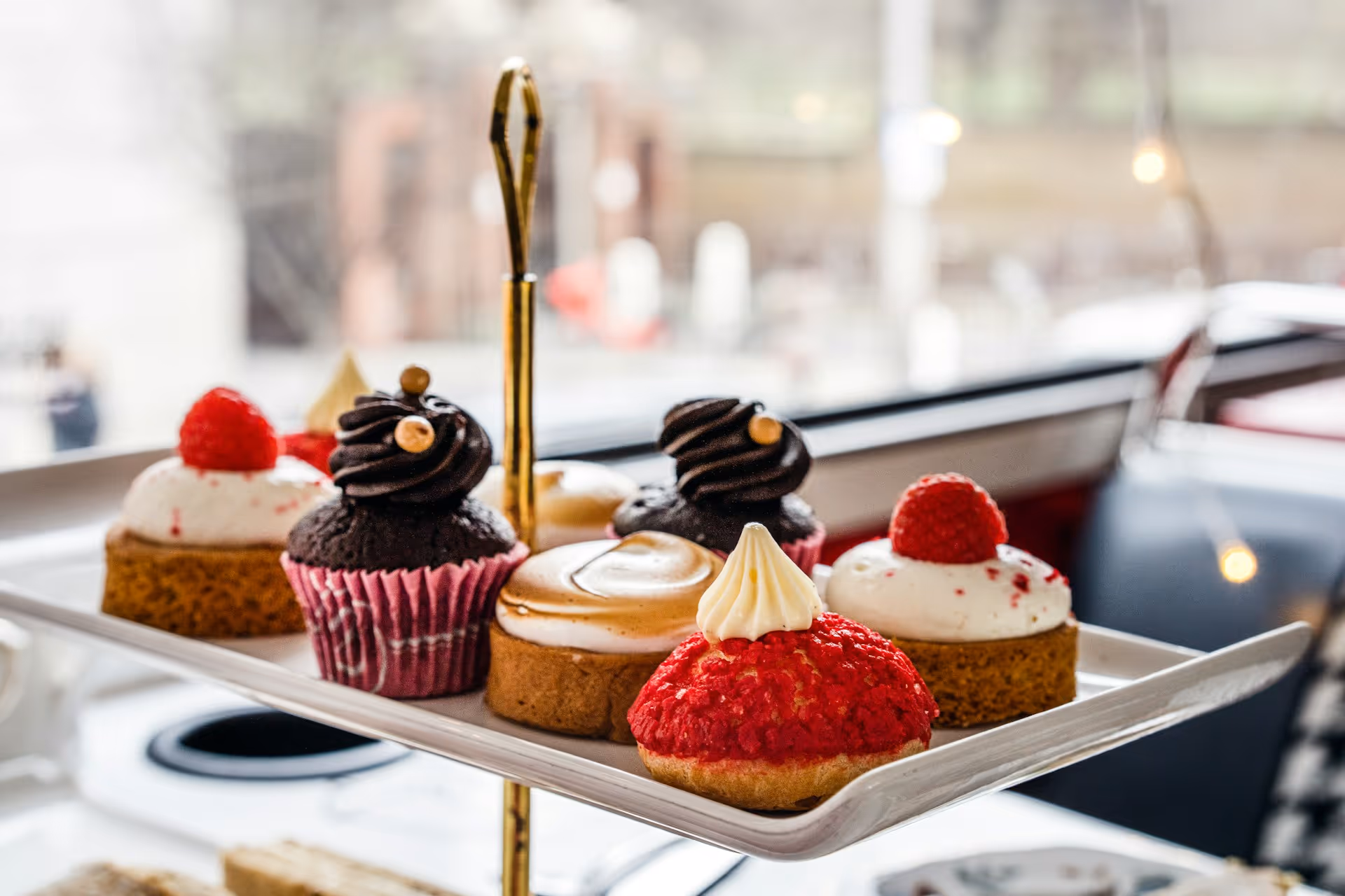A tiered high tea stand with an assortment of pastries, cupcakes, raspberry-topped tarts, and cream-filled choux buns.